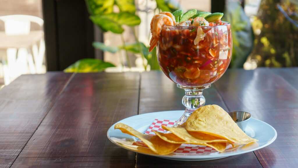 Vibrant shrimp cocktail served in a glass with tortilla chips on a wooden table.